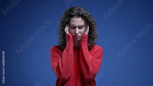 Anxious young woman with holding head temples with hands struggling with mental anxiety feeling overwhelmed with problems standing on blue background © Marco