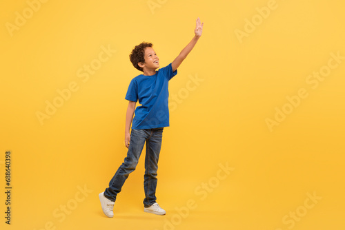 Black boy reaching up, blue tee, yellow background