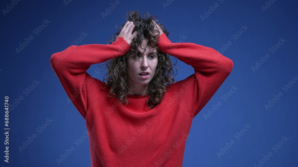 Frustrated young woman pulling her hair in anxiety and desperation on blue backdrop with red sweater. Anxious 20s female person Frustrated young woman pulling her hair in anxiety and desperation on blue backdrop with red sweater. Anxious 20s female person