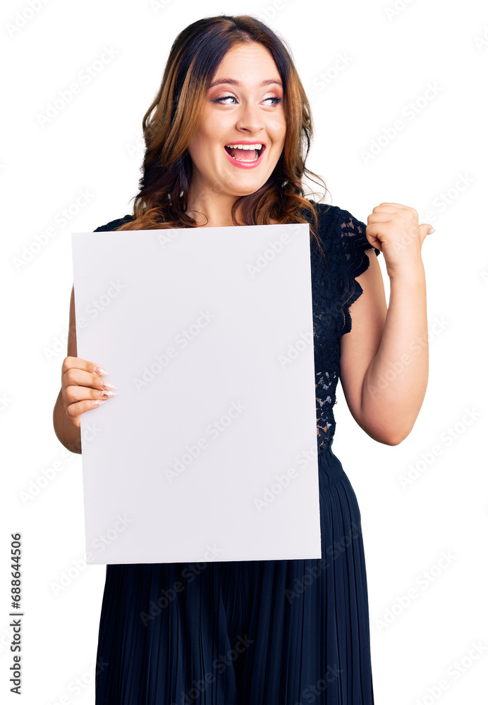 Young beautiful caucasian woman holding cardboard banner with blank space pointing thumb up to the side smiling happy with open mouth Young beautiful caucasian woman holding cardboard banner with blank space pointing thumb up to the side smiling happy with open mouth