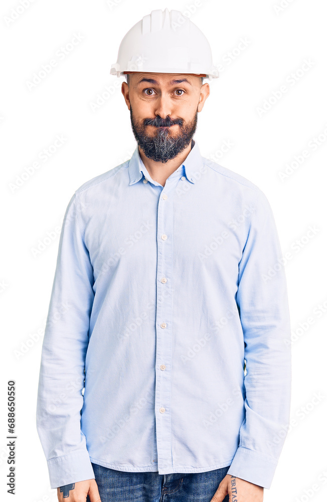 Young handsome man wearing architect hardhat puffing cheeks with funny face. mouth inflated with air, crazy expression. Young handsome man wearing architect hardhat puffing cheeks with funny face. mouth inflated with air, crazy expression.
