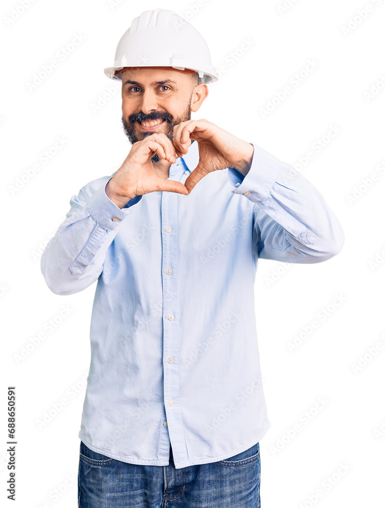 Young handsome man wearing architect hardhat smiling in love doing heart symbol shape with hands. romantic concept.