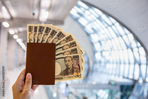 Hand holding a passport with ten thousand Japanese yen bills at the airport. Copy space background photo