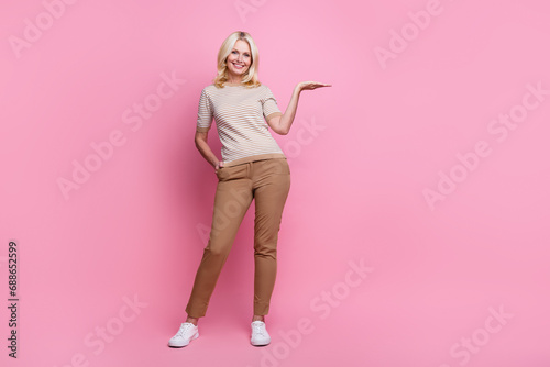 Full size photo of positive person dressed striped t-shirt pants palm presenting sale empty space isolated on pink color background