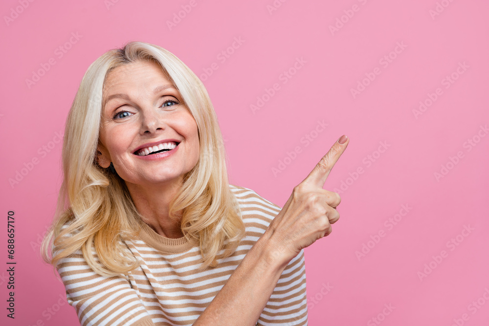 Photo of pleasant person with blond hair dressed striped t-shirt indicating at discount empty space isolated on pink color background Photo of pleasant person with blond hair dressed striped t-shirt indicating at discount empty space isolated on pink color background