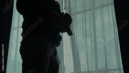 Mysterious man wearing black hoodie holding a pistol wearing a cloth mask covering his face completely in front of the door, Silhouette and dark concept image,threat of firearms,attack or defense.