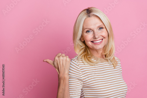 Photo of cheerful person with blond hairstyle dressed striped t-shirt indicating at discount empty space isolated on pink color background