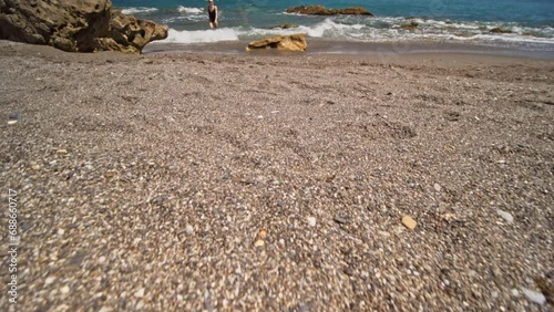 Tourist attractive woman in swimwear walks along the empty beach on a beautiful sunny day. Female tourist on summer vacation