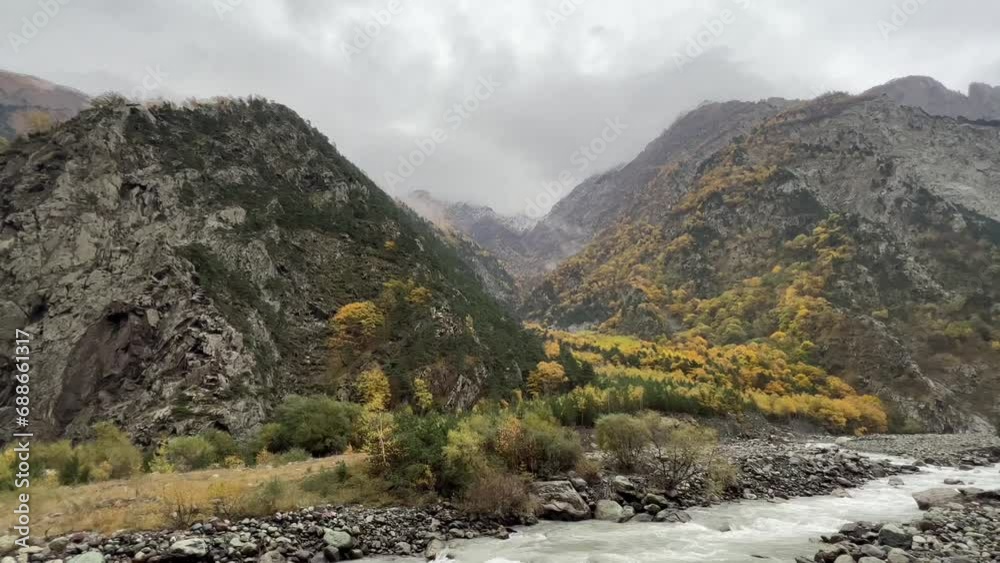 Rugged mountain landscape with autumn foliage and a flowing river, set under an overcast sky Rugged mountain landscape with autumn foliage and a flowing river, set under an overcast sky