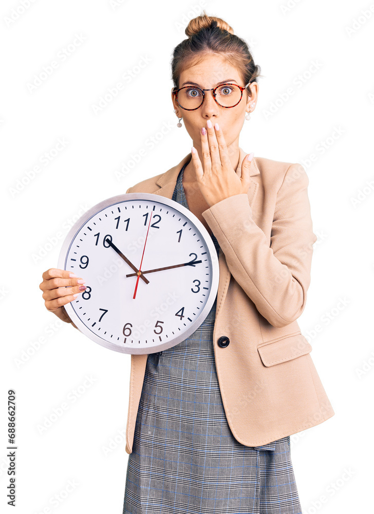 Beautiful caucasian woman with blonde hair wearing business jacket and holding clock covering mouth with hand, shocked and afraid for mistake. surprised expression Beautiful caucasian woman with blonde hair wearing business jacket and holding clock covering mouth with hand, shocked and afraid for mistake. surprised expression