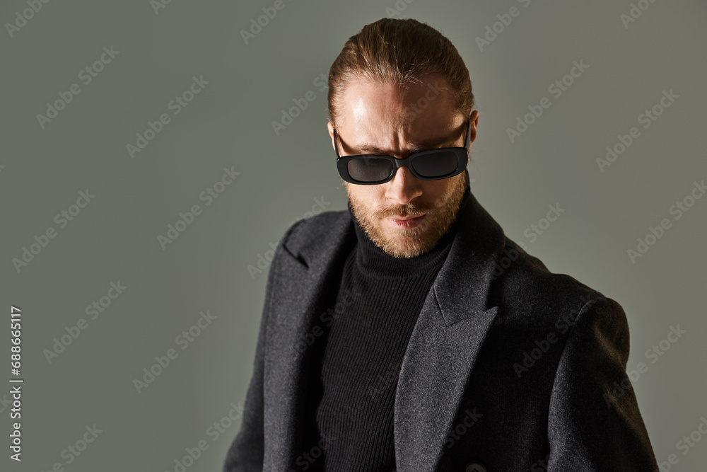 portrait of handsome bearded man in trendy sunglasses and black attire posing on grey backdrop portrait of handsome bearded man in trendy sunglasses and black attire posing on grey backdrop