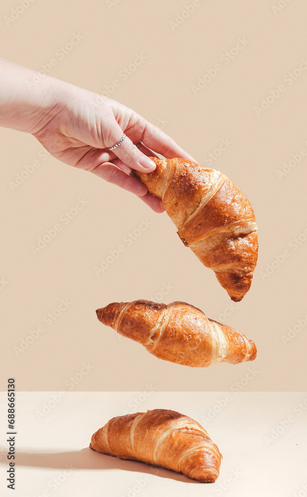 Fresh delicious croissants are held by a female hand, levitation.