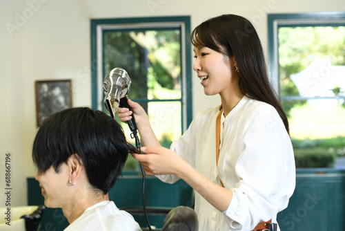 男性客の髪をドライヤーで乾かすアジア人の女性美容師