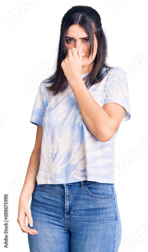 Young beautiful girl wearing casual t shirt smelling something stinky and disgusting, intolerable smell, holding breath with fingers on nose. bad smell