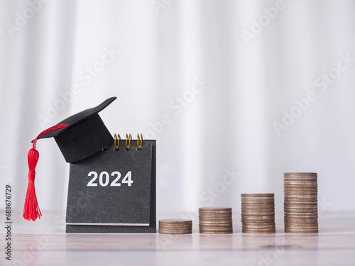 Study goals, 2024 Desk calendar with graduation hat and stack of coins. The concept of saving money for education, student loan, scholarship, tuition fees in New Year 2024