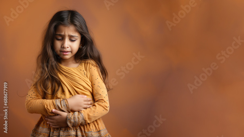 Indian little girl wincing in pain and hand rubbing stomach