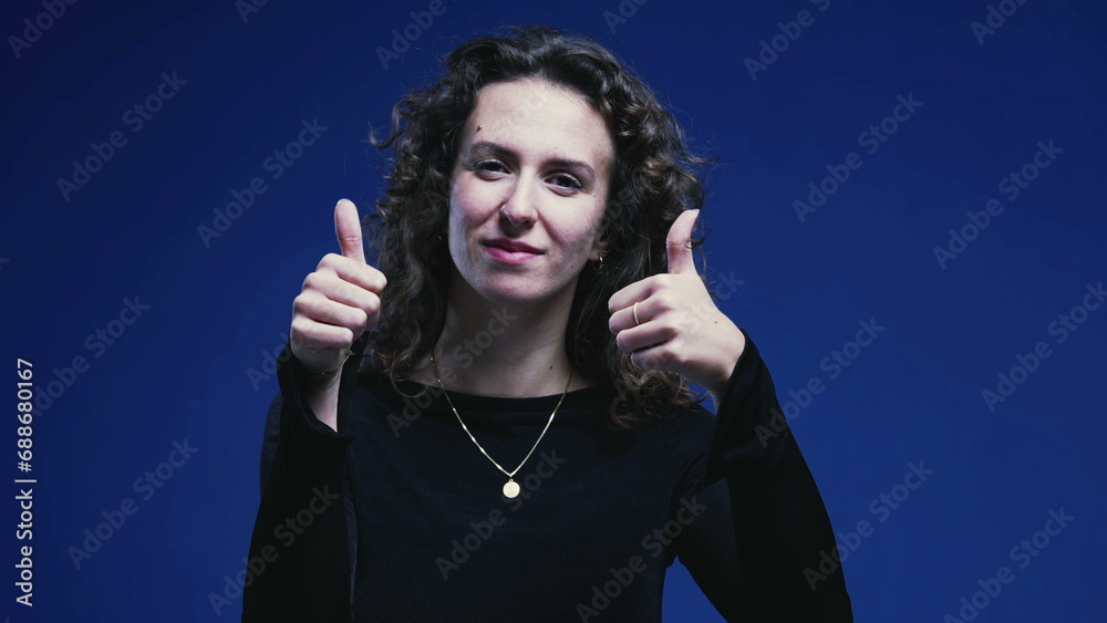 Positive Young Woman Giving Thumbs Up, Blue Background Signifying Approval Positive Young Woman Giving Thumbs Up, Blue Background Signifying Approval