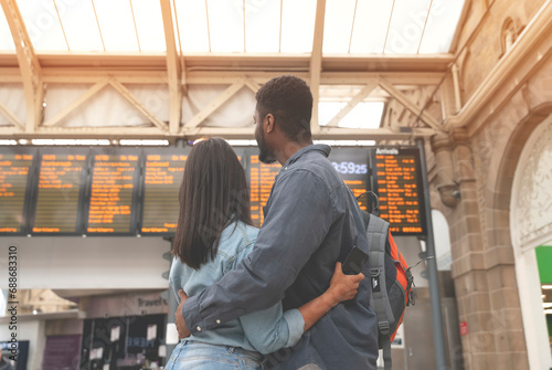 Happy man and woman in love waiting for a train and cuddle at a railway station in front of the timetable toned image photo