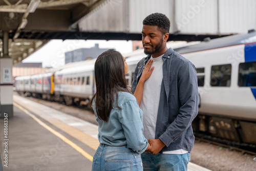 Happy man and woman in love waiting for a train and talking at a railway station platform