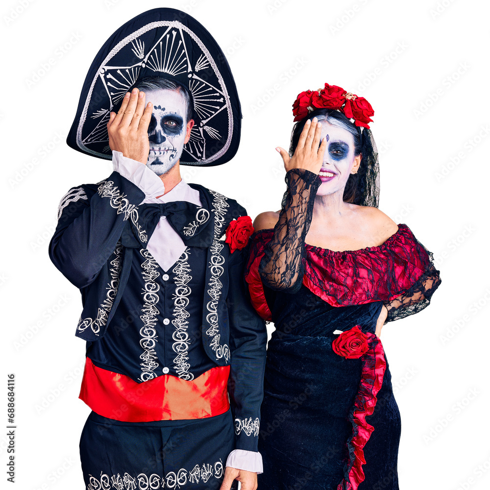Young couple wearing mexican day of the dead costume over background covering one eye with hand, confident smile on face and surprise emotion.