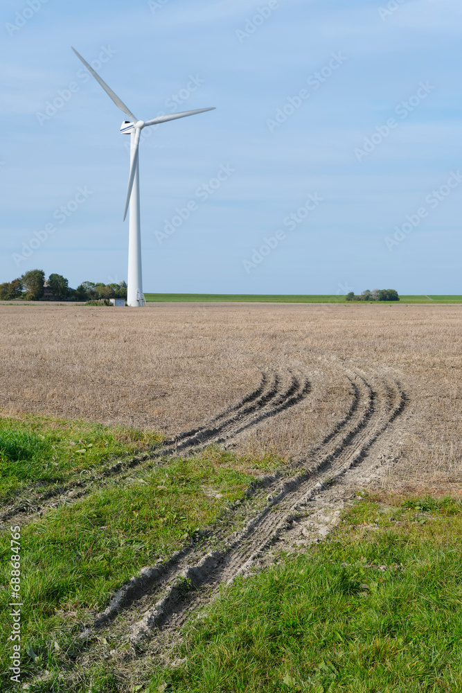 Wind turbine in a just harvested field with tractor tracks under a blue sky. Concept of clean energy. Wind turbine in a just harvested field with tractor tracks under a blue sky. Concept of clean energy.