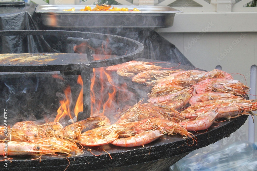 Seafood slices are cooked on a fire pit surface in the shape of cone shaped bowl. Bowl-shaped flat grill with prawns and shrimps. Outdoor barbecue cooking. Street food concept. Toast the hot grilled