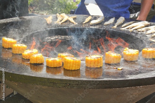 Fresh grilled corn on the cob. Summer food. Vegetarian dish barbecue and grill. Outdoor barbecue cooking. Picnic on backyard on open air. Street food concept. Grilled corn on bowl-shaped flat grill