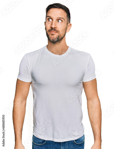 Handsome man with beard wearing casual white t shirt smiling looking to the side and staring away thinking.