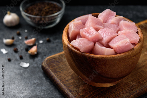 Diced raw chicken breast in wooden bowl on black background.