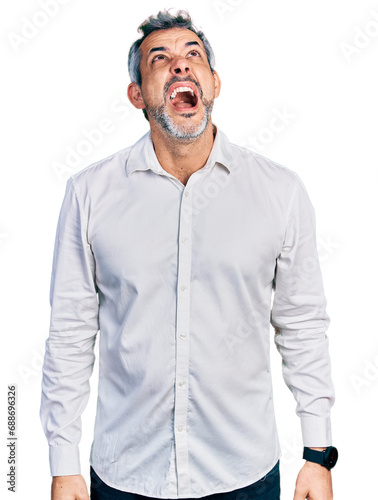 Middle age hispanic with grey hair wearing casual white shirt angry and mad screaming frustrated and furious, shouting with anger. rage and aggressive concept.
