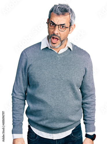 Middle age hispanic with grey hair wearing glasses in shock face, looking skeptical and sarcastic, surprised with open mouth photo