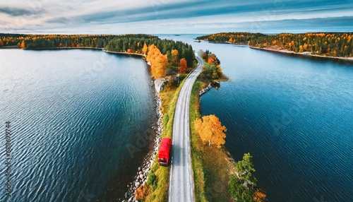 aerial view of fall road and blue water lake sea ocean red car with a roof rack on a country road in finland