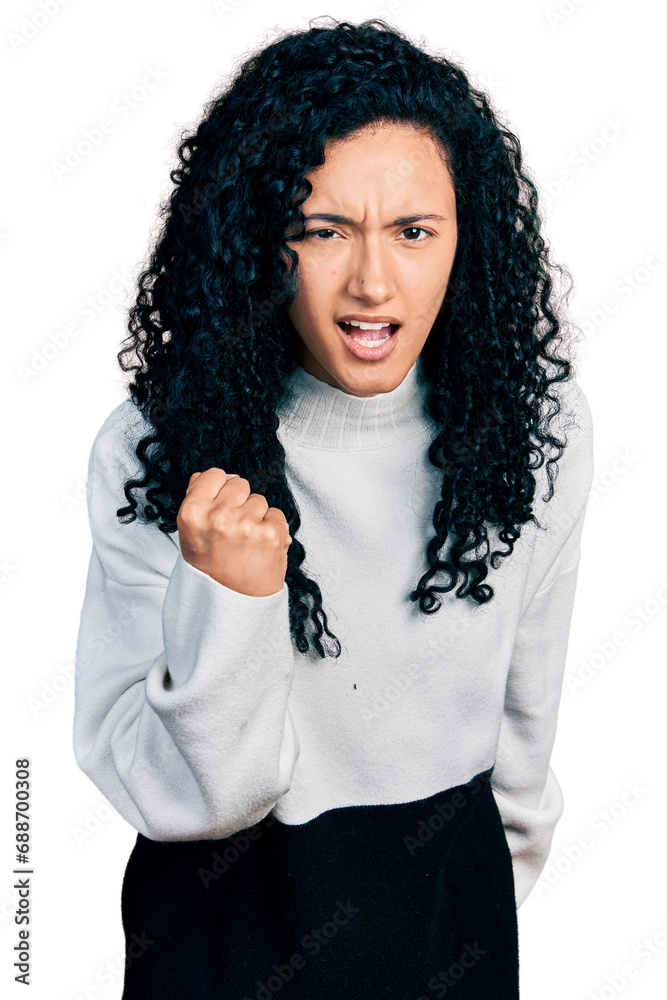 Young hispanic woman with curly hair wearing casual sweater angry and mad raising fist frustrated and furious while shouting with anger. rage and aggressive concept. Young hispanic woman with curly hair wearing casual sweater angry and mad raising fist frustrated and furious while shouting with anger. rage and aggressive concept.