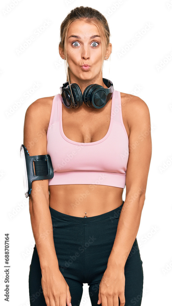 Young blonde woman wearing gym clothes and using headphones making fish face with lips, crazy and comical gesture. funny expression. Young blonde woman wearing gym clothes and using headphones making fish face with lips, crazy and comical gesture. funny expression.