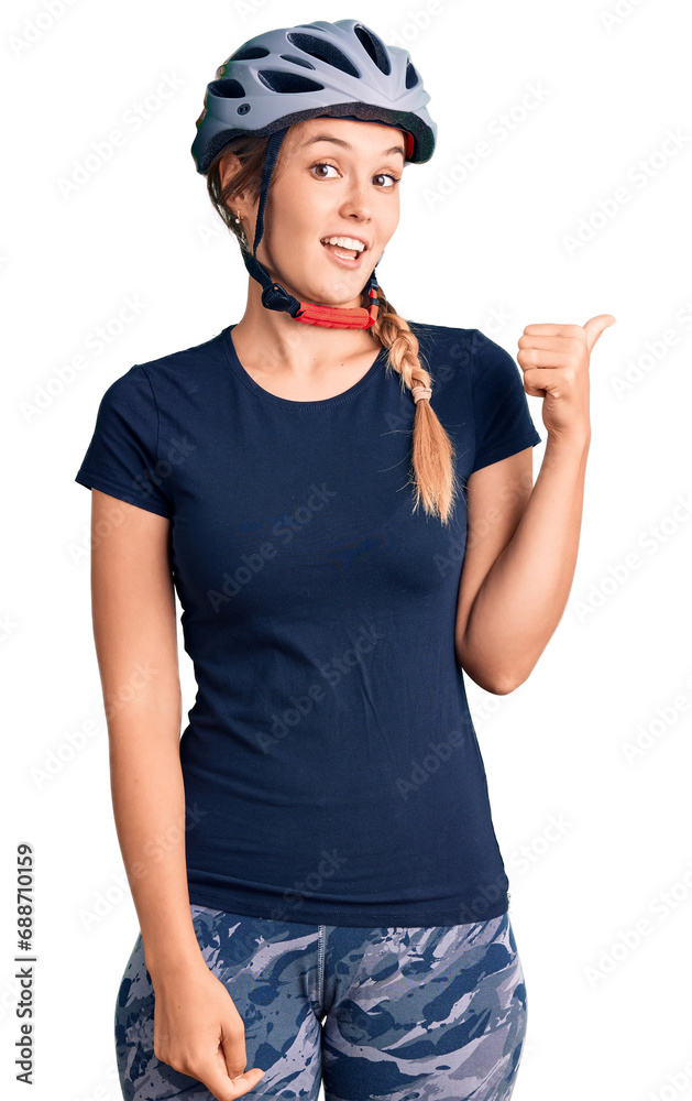 Beautiful caucasian woman wearing bike helmet smiling with happy face looking and pointing to the side with thumb up. Beautiful caucasian woman wearing bike helmet smiling with happy face looking and pointing to the side with thumb up.