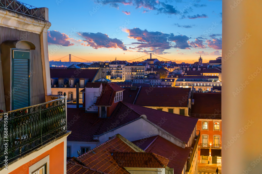A colorful dramatic sunset sky over the cityscape and Ponte 25 de Abril bridge seen from the hillside medieval Alfama district in Lisbon Portugal.