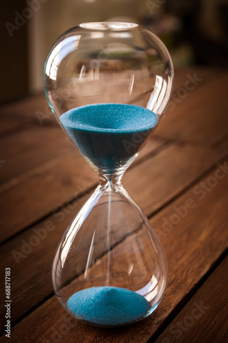 Hourglass containing blue sand on a rustic wooden board