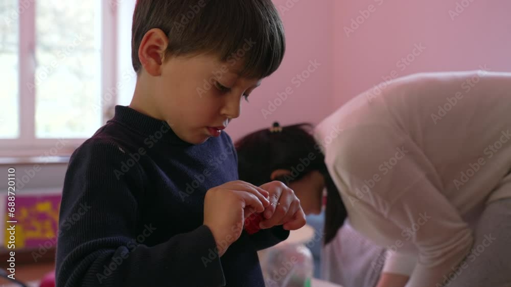 Child preparing to decorate Christmas tree with ball ornament during holiday season, young boy trying to put hook into ball Child preparing to decorate Christmas tree with ball ornament during holiday season, young boy trying to put hook into ball