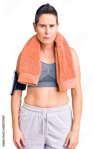 Young woman with short hair wearing sportswear and towel using smartphone skeptic and nervous, frowning upset because of problem. negative person.