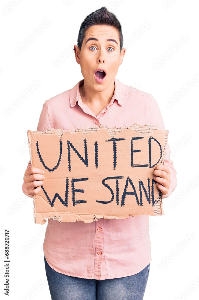 Young woman with short hair holding united we stand banner scared and amazed with open mouth for surprise, disbelief face Young woman with short hair holding united we stand banner scared and amazed with open mouth for surprise, disbelief face