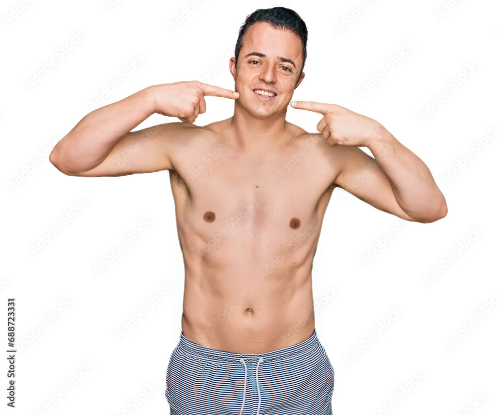 Handsome young man wearing swimwear shirtless smiling cheerful showing and pointing with fingers teeth and mouth. dental health concept.