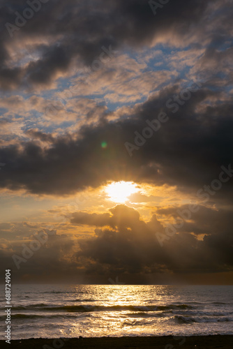 Sunset view  seashore  stormy waves  heavy rain clouds on horizon  sun breaking through the cloud like an eye. Vertical photo