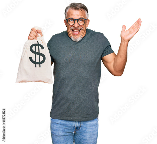 фотографія Middle age grey-haired man holding dollars bag celebrating victory with happy sm