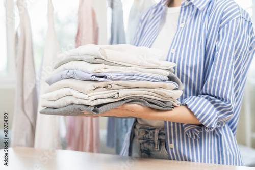 Feel softness, chore of pretty asian young woman hand holding pile clothing from table, stack folding clean clothes after washing, laundry and dry. Household working at home. Laundry of maid concept. photo