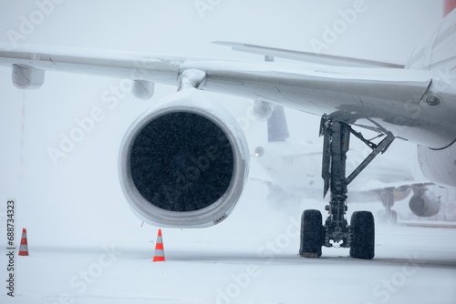 Traffic at airport during heavy snowfall. Snowflakes against jet engine and taxiing airplane at airport taxiway during frosty winter day. Extreme weather in transportation..