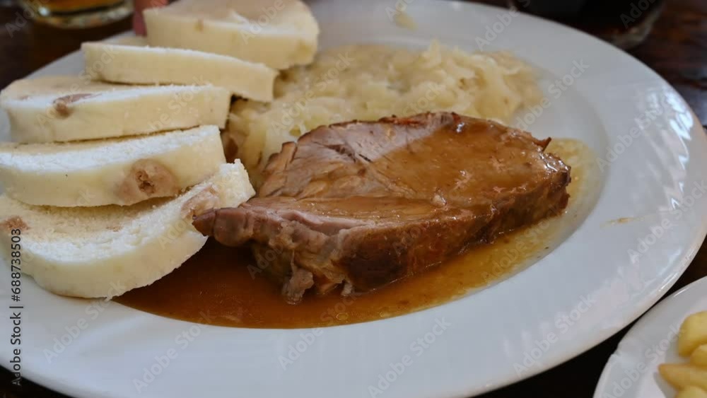 Prague, Czech Republic, August 4,2023. Close-up with one of the typical dishes: stewed pork with sauerkraut and bread for dipping. A side dish of chips, mugs of light and dark beer. The hand grabs Prague, Czech Republic, August 4,2023. Close-up with one of the typical dishes: stewed pork with sauerkraut and bread for dipping. A side dish of chips, mugs of light and dark beer. The hand grabs