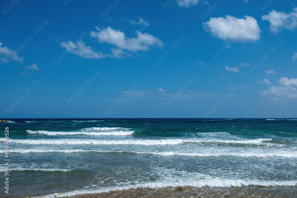 Greek sandy beach. Ripple dark sea water, white foam, blue sky with cloud background, copy space.
