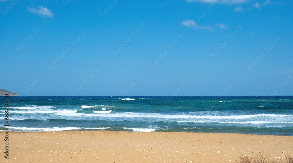Greek sandy beach. Ripple dark sea water, white foam, blue sky with cloud background, copy space.
