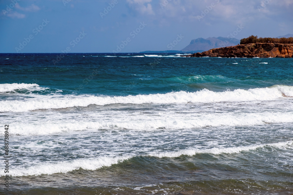 Greece ripple dark sea, splashing foam, part of rocky Greek island, blue sky with cloud background.