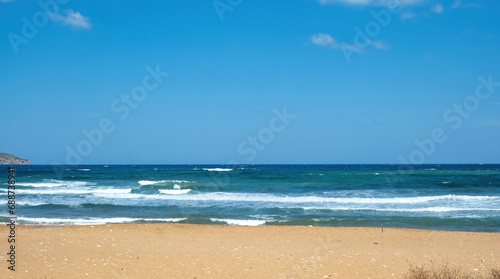 Greek sandy beach. Ripple dark sea water  white foam  blue sky with cloud background  copy space.